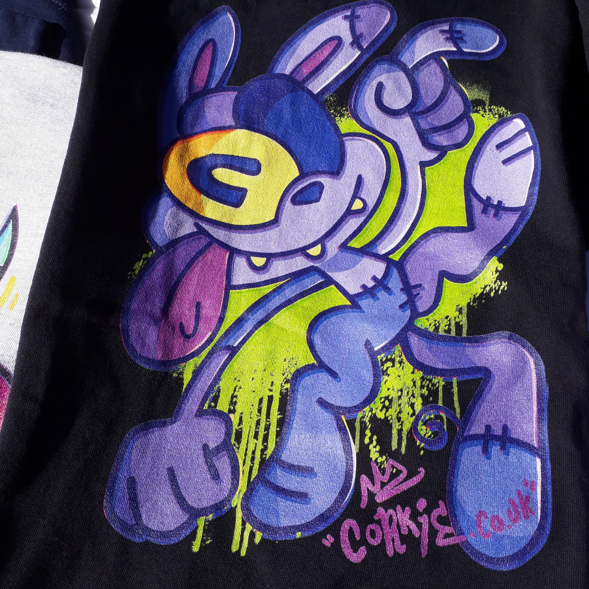 Purple monster graffiti character by streetwear brand CORKiE, printed onto a black shirt with a spray paint effect in the background.