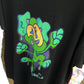 Green slime graffiti character by streetwear brand CORKiE, printed onto a black shirt with a spray paint effect in the background.