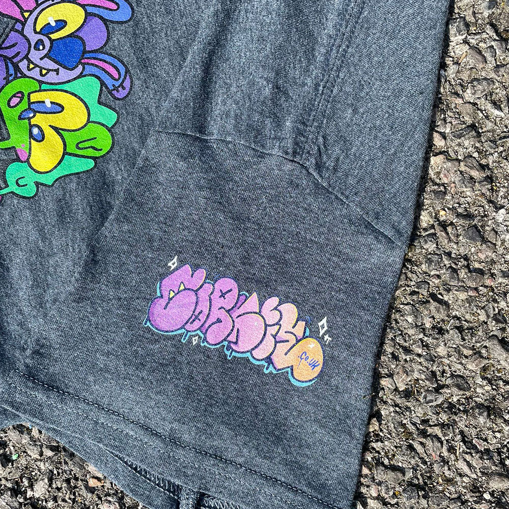 Clouse up of throwie tag on Indie streetwear brand CORKiE grey t-shirt. Featuring a graphic design with two retro graffiti style characters in the shirts pocket. With a throwie bubble text logo on the sleeve.